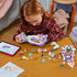 LEGO Disney Princess Ariel's Royal Wedding Boat pieces in white, lavender, pink, and teal plastic cover a table as a child assembles the modular boat beside a tablet.