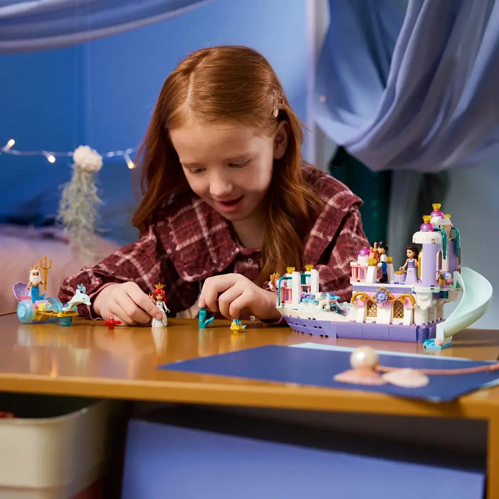 LEGO Disney Princess Ariel's Royal Wedding Boat in white, lavender, pink, and teal plastic sits on a table as a child plays with Ariel, sea figures, and the wheeled chariot.