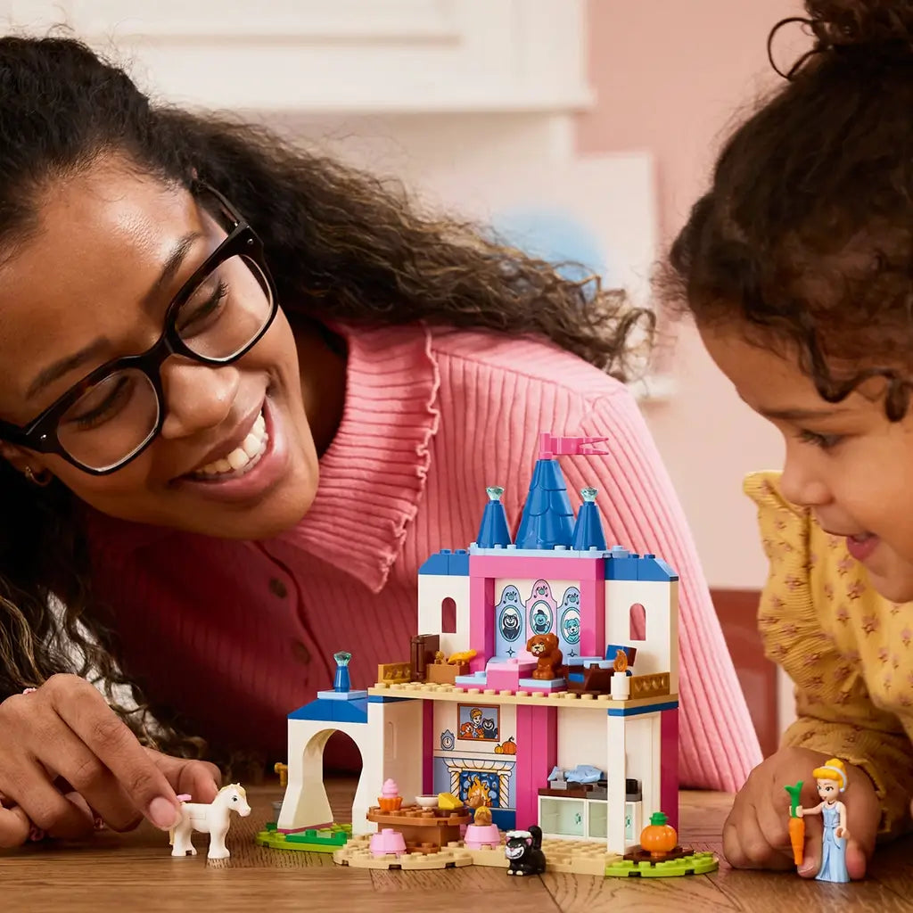 LEGO Disney Princess Cinderella Animal Friends Castle in blue, pink, and white plastic is explored by an adult and child, with Cinderella, horse, cat, and carrot nearby.