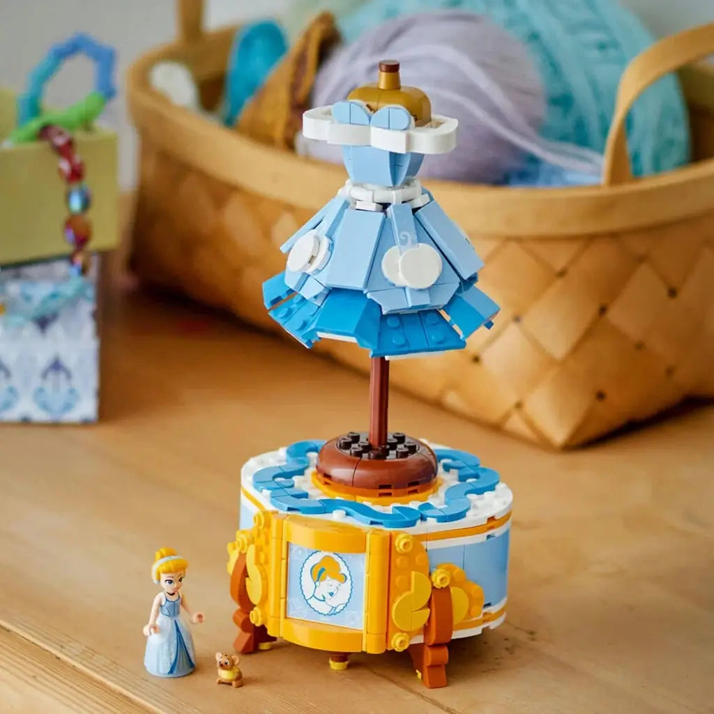 LEGO Disney Princess Cinderella dress display in light blue, white and gold plastic with mannequin-style gown above a decorative cabinet, beside Cinderella and mouse figures on a wooden tabletop.