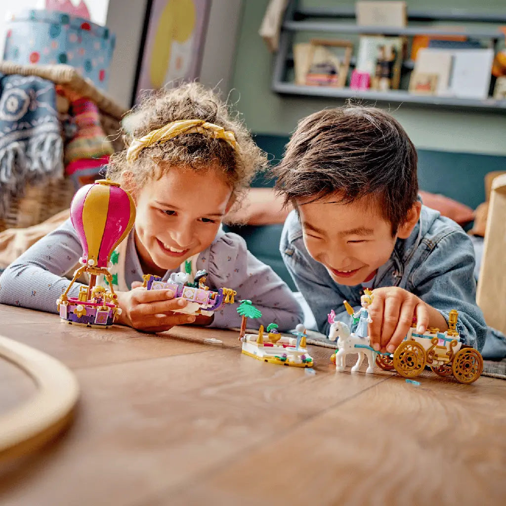 LEGO Disney Princess playset in pink, purple, gold and white plastic shows two children playing with a balloon, carriage, flying carpet and figures on a wooden table.