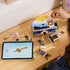 LEGO Disney Princess Jasmine's Jewelry Box pieces in teal, lavender, white, and gold plastic cover a wood table as a child builds the box beside digital instructions on a tablet.
