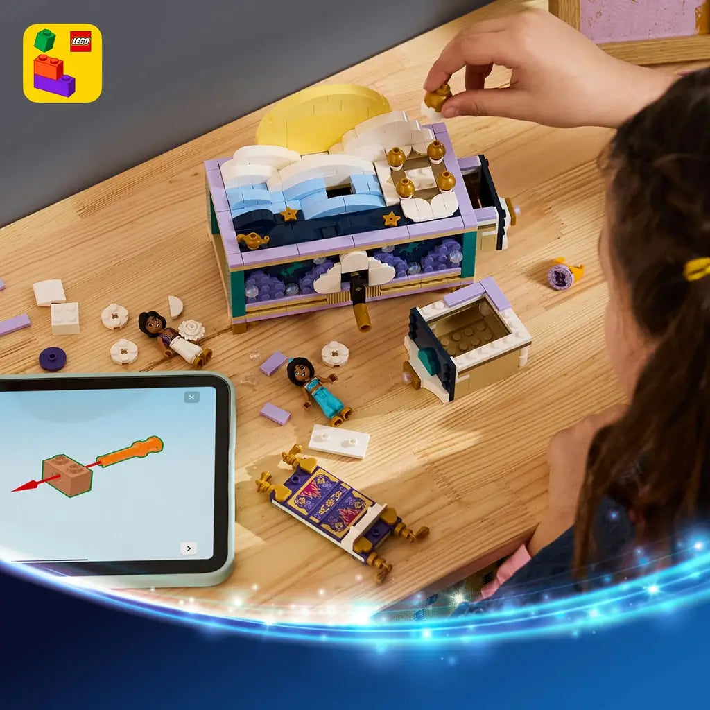 LEGO Disney Princess Jasmine's Jewelry Box in teal, lavender, white, and gold plastic sits partly assembled on a wood table as a child builds beside tablet instructions and figures.