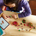 LEGO Disney Moana Kakamora building set in brown, pink, green, and tan plastic is assembled by a child on a wood table with loose tropical pieces and tablet instructions nearby.