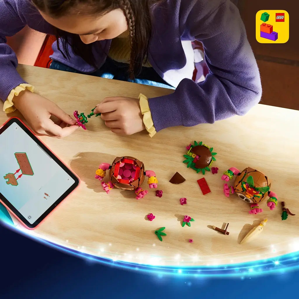 LEGO Disney Moana Kakamora set pieces in brown, pink, green, and tan plastic cover a wood table as a child builds floral accessories beside tablet instructions and two warriors.