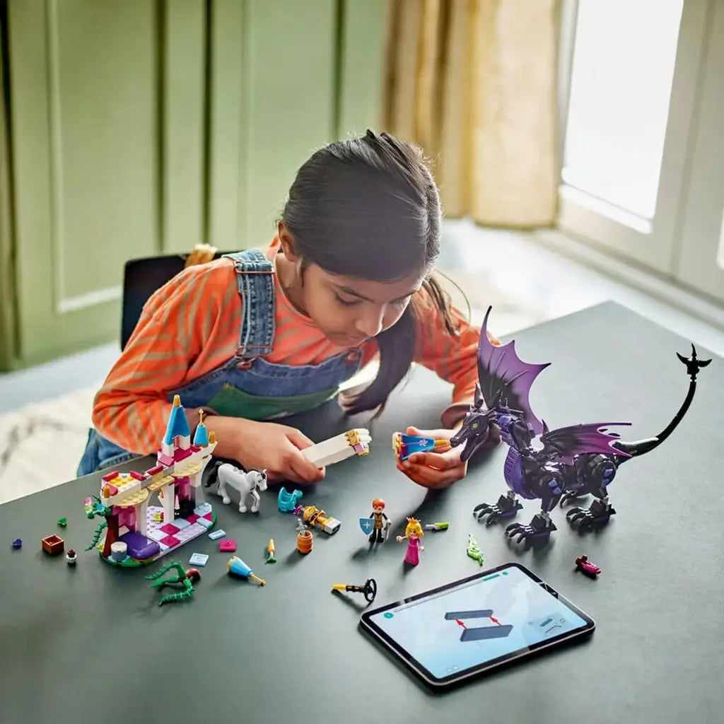 LEGO Disney Princess Maleficent's Dragon Form set in colorful plastic as a child assembles the castle, dragon and character figures beside a tablet showing digital building instructions.