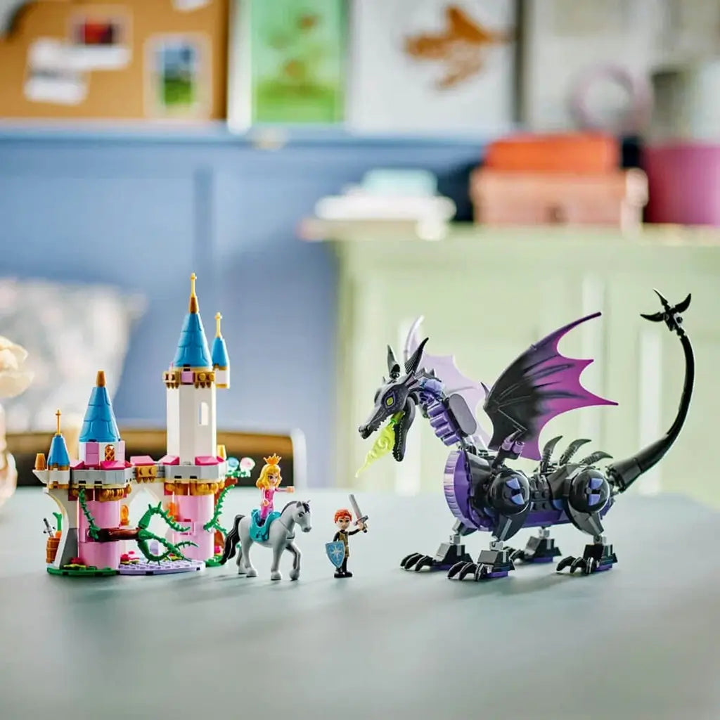 LEGO Disney Princess Maleficent's Dragon Form display with black and purple dragon, pink castle and character figures arranged on a tabletop in a bright indoor room.