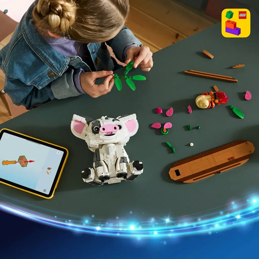 LEGO Disney Moana Pua building set in white, gray, pink, green, and brown plastic is assembled by a child at a table with digital instructions, loose pieces, Heihei, and brown base.