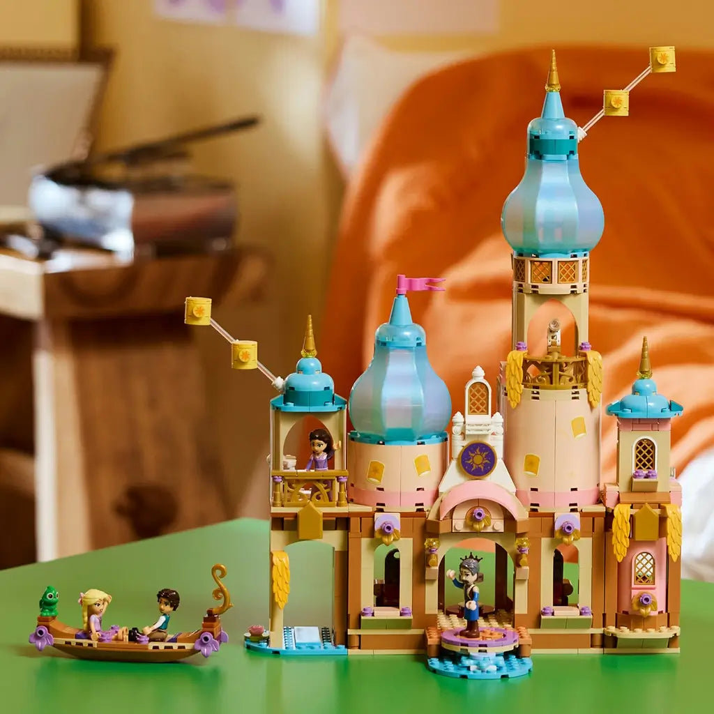 LEGO Disney Princess Rapunzel's Castle in tan, pink, turquoise, and gold plastic is displayed on a green table with tall domed towers, character figures, and a small boat.
