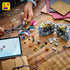 LEGO Disney Sally flowerpot build scene shows colorful plastic pieces including blue cauldron halves, black stems, purple bell flowers, and multicolor petals arranged on a wooden table during assembly with tools and instructions nearby.