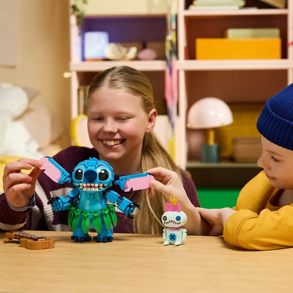LEGO Disney Stitch and Scrump set in blue, pink, green, and tan plastic is played with by two smiling children at a table, with Stitch, Scrump, and a guitar.