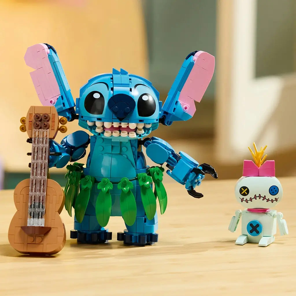 LEGO Disney Stitch and Scrump figures in blue, pink, green, and tan plastic stand on a wooden table beside a brown guitar, with Stitch wearing a leafy hula skirt.
