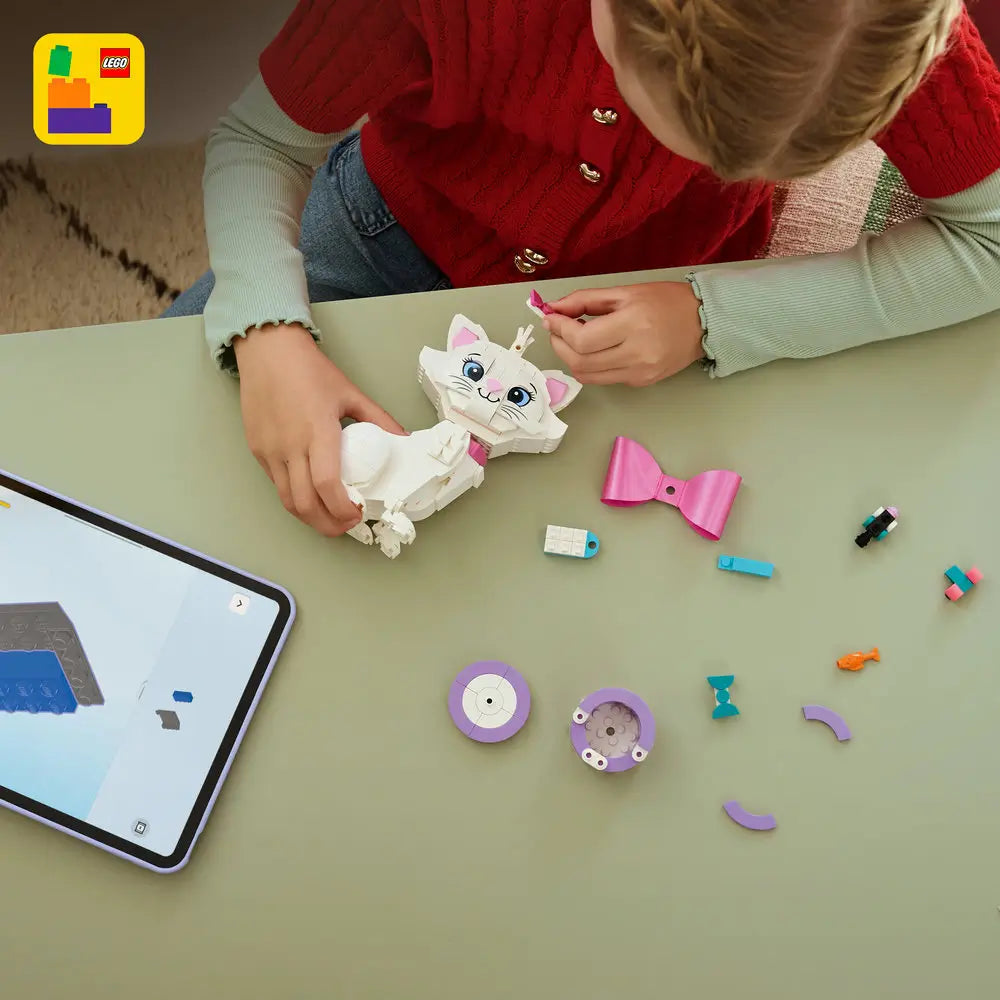 LEGO Disney Aristocats Marie playset shown during building, with white and pink plastic cat parts, bow accessories, loose pieces, and a child assembling the figure on a tabletop using digital instructions.