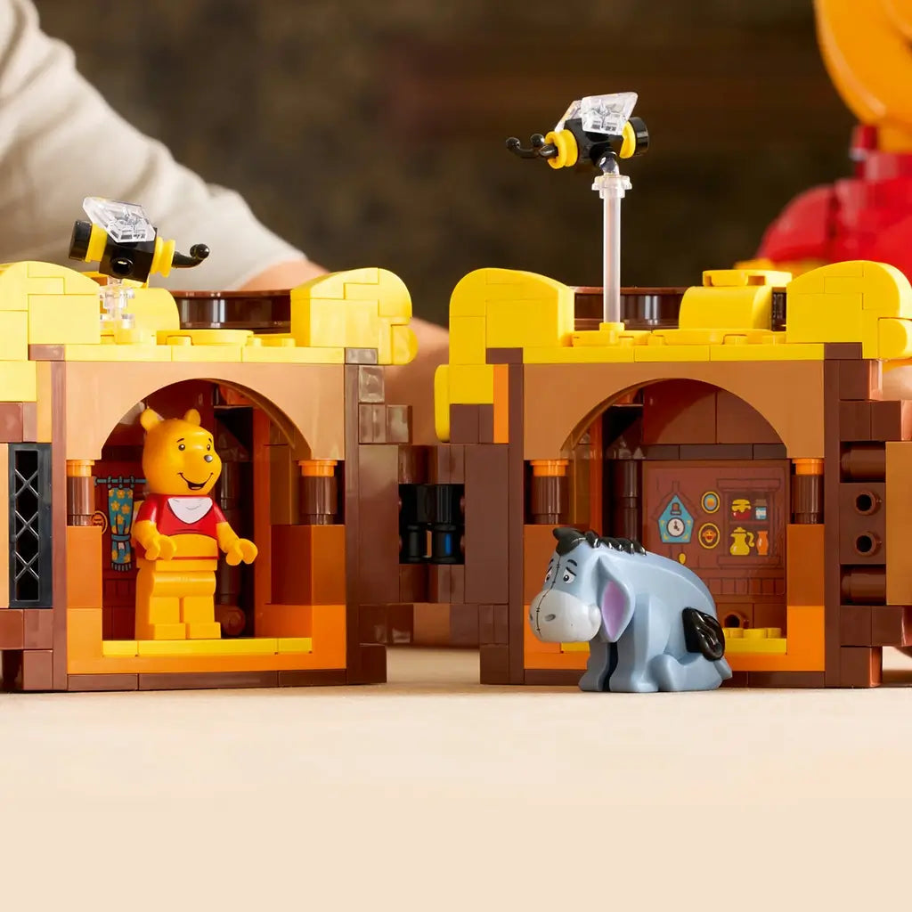 LEGO Disney Winnie the Pooh close-up in yellow and brown plastic, honey pot with dripping honey and small bees, detailed scene with mini Pooh and Eeyore figures in a cozy setting.