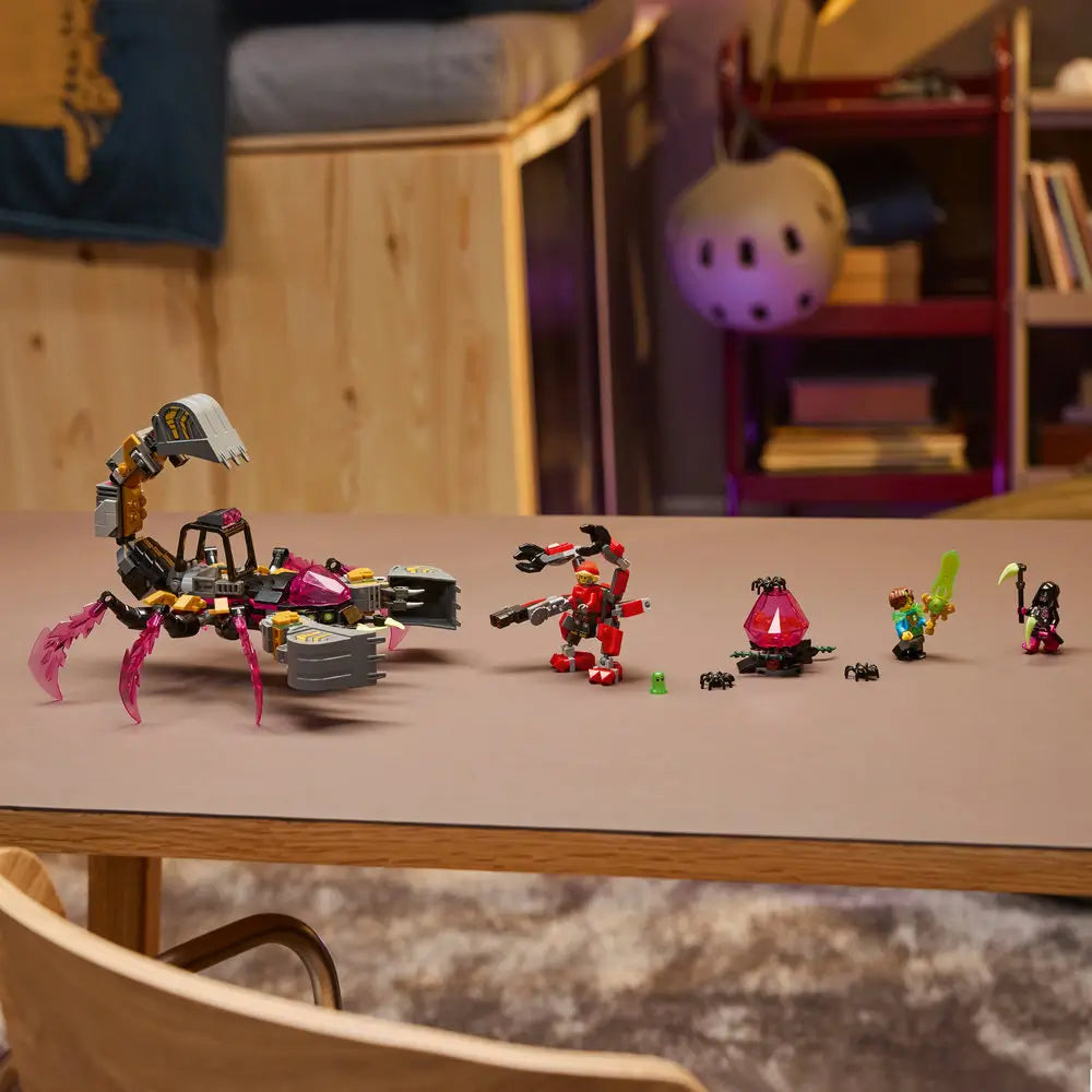 LEGO DREAMZzz Nightmare Scorpion Digger displayed on table in dark gray and gold plastic with pink crystal claws, minifigures lined up, and imaginative fantasy play setting indoors.