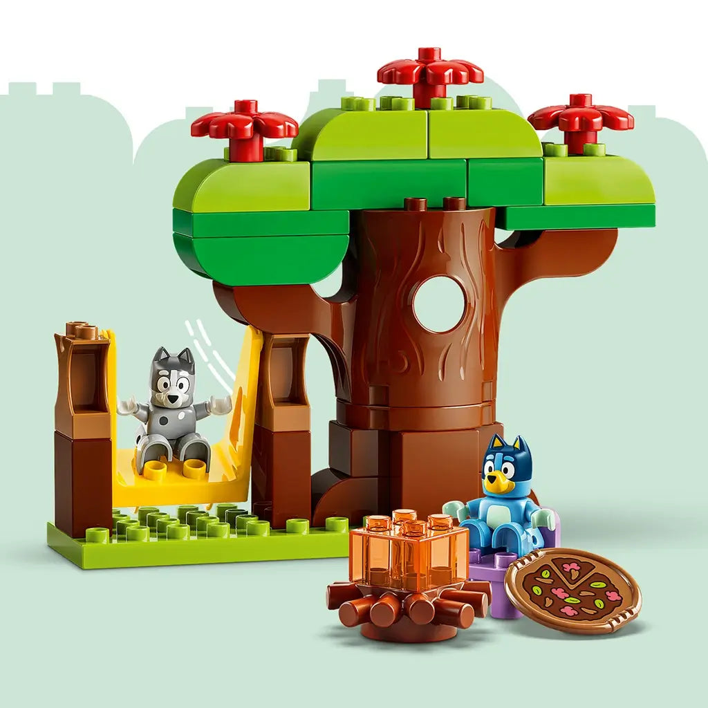 LEGO DUPLO Bluey Pizza Girls playset features a brown and green plastic tree with yellow swing, campfire and pizza, while Bluey and Muffin figures sit nearby.