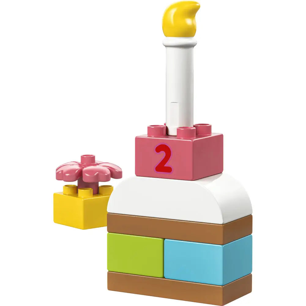 LEGO DUPLO celebration cake toy, pastel yellow, white, brown, green, and blue plastic bricks with a smooth chunky texture, stacked square cake shape topped with a white candle and flower accent, displayed on a clean white background.