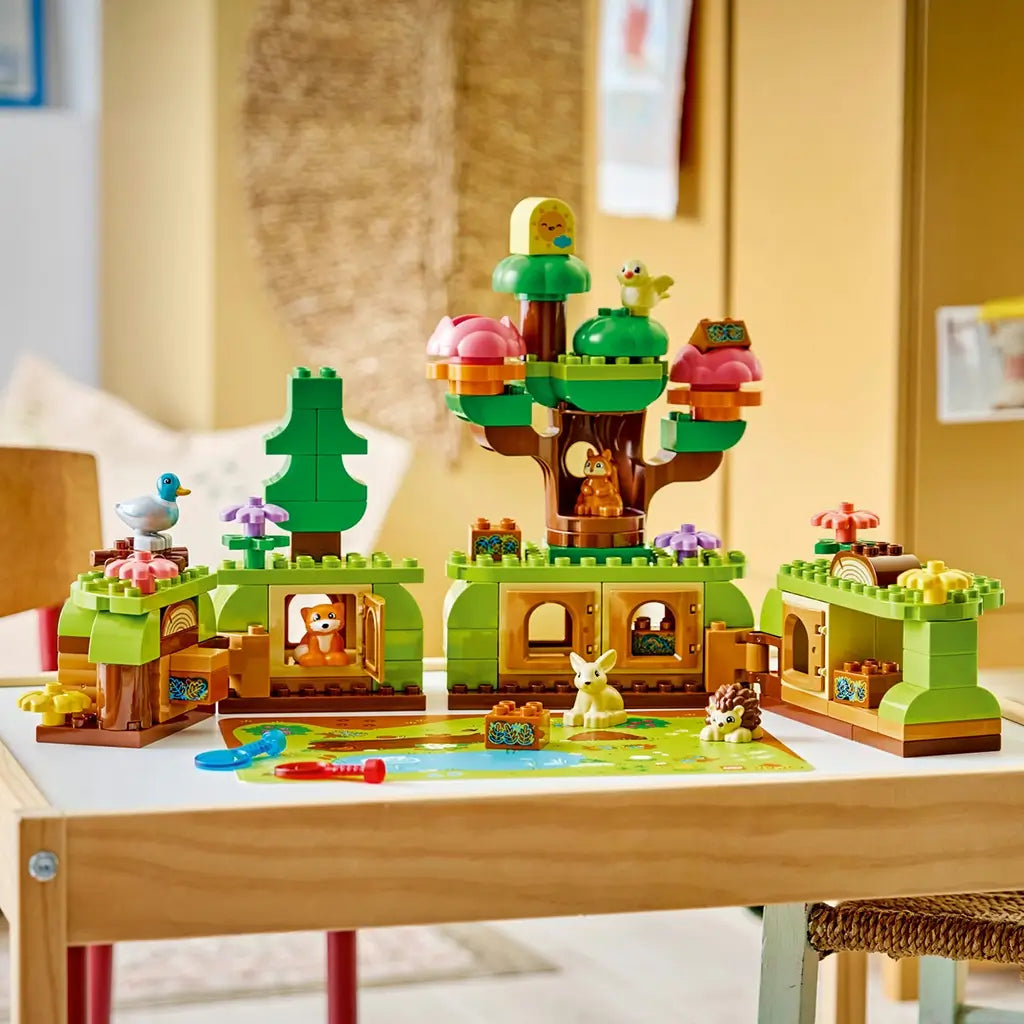 LEGO DUPLO Discovery Forest playset displays green and brown forest habitats, pink and purple flowers, five wild animal figures, red and blue magnifiers on a wooden table.