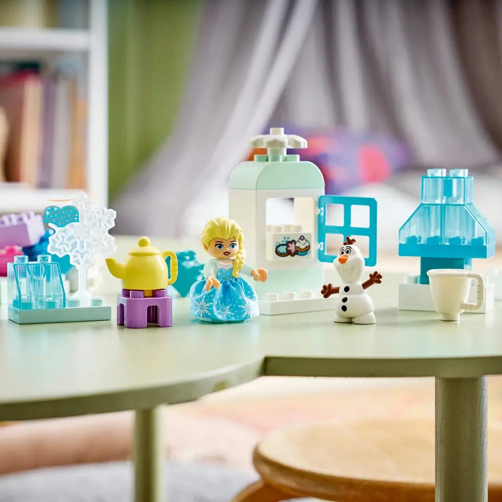 LEGO DUPLO Disney Frozen playset displays aqua, white and pastel plastic builds with Elsa, Olaf, a yellow teapot, cup and icy accessories on a green table.