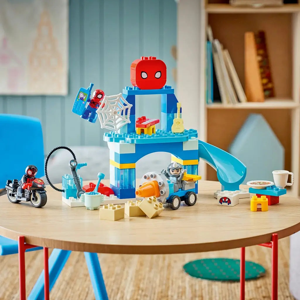 LEGO DUPLO Marvel Spidey Webquarters playset features a blue plastic headquarters with slide, web, vehicles, figures and accessories displayed on a wooden table.