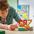 LEGO Cristiano Ronaldo soccer display in red, green, gold and white plastic bricks, compact CR7 highlight model being adjusted by a builder on a tabletop in a bright indoor environment.