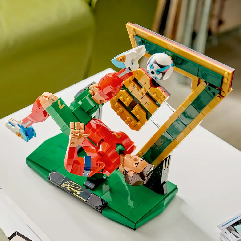 LEGO Cristiano Ronaldo soccer model features red, green, gold and black plastic brick construction posed in an overhead bicycle kick with a floating ball, CR7 backdrop and display base on a tabletop.