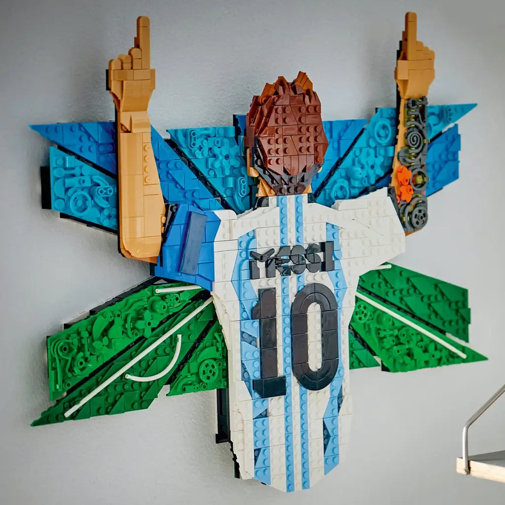 LEGO Lionel Messi wall décor features white, sky-blue and green textured plastic brick elements forming a number 10 Argentina jersey celebration scene with raised arms displayed prominently on an interior wall.