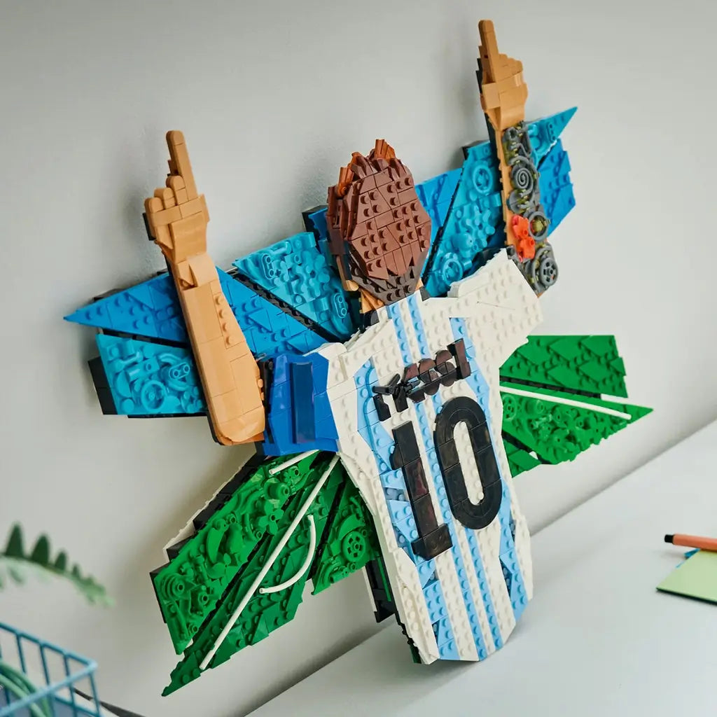 LEGO Lionel Messi collectible wall art features white, sky-blue and green plastic brick construction shaped as the number 10 Argentina jersey celebration display, mounted above a shelf in a modern room.