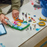LEGO Lionel Messi soccer set in blue, green, white and gold plastic bricks, partially assembled with loose components, minifigure and digital instructions spread across a tabletop workspace.