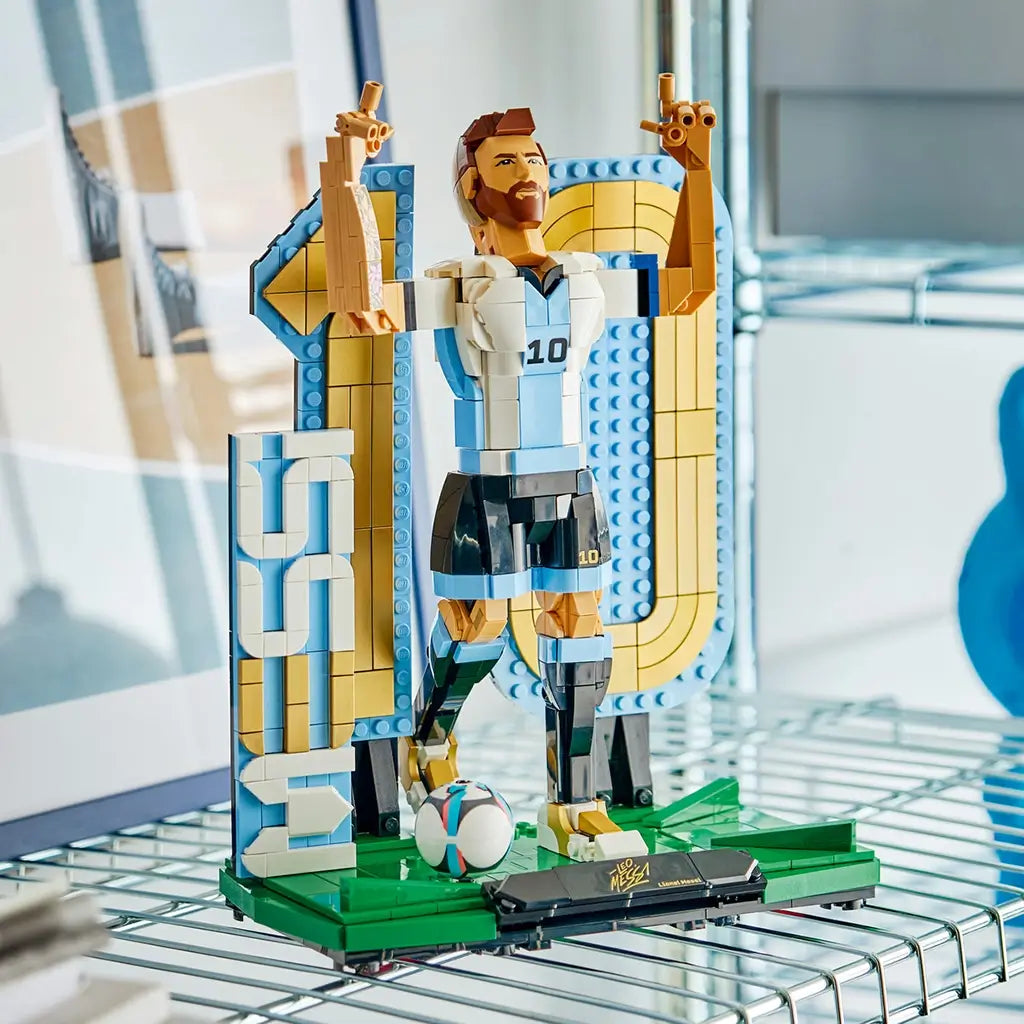 LEGO Lionel Messi soccer display features light blue, white, black, gold and green plastic brick construction showing the football icon with raised arms, number 10 backdrop and ball in a room setting.