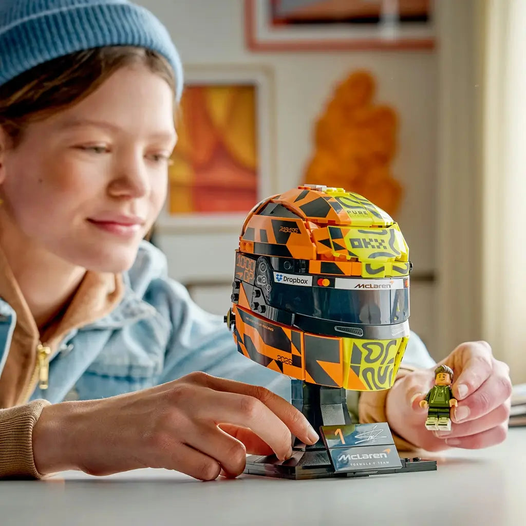 LEGO McLaren Formula 1 helmet set shows yellow, orange and black plastic pieces with curved racing-helmet panels being assembled beside a tablet guide, creating a detailed Lando Norris display model.