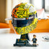 LEGO McLaren Formula 1 helmet display features yellow, orange and black plastic panels with bold racing graphics, a dark visor and Lando Norris minifigure showcased on a stand in a bright room setting.