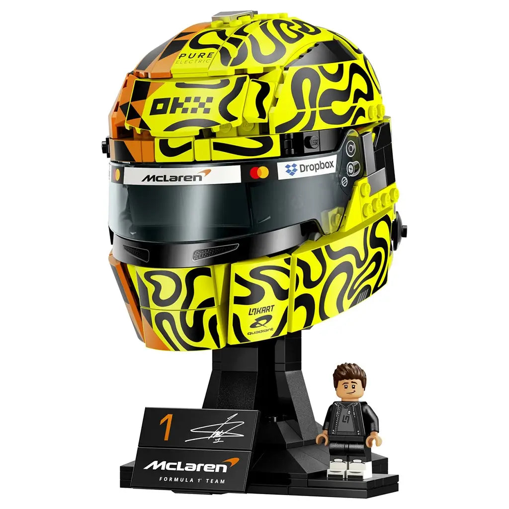 LEGO McLaren Formula 1 helmet collectible features bright yellow, orange and black plastic panels with racing-inspired graphics, a dark visor, display stand and Lando Norris minifigure on a studio background.