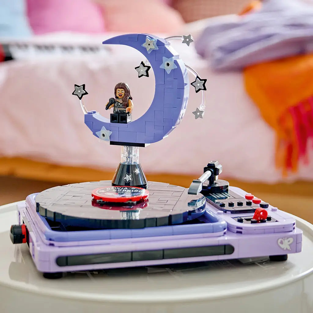 LEGO Olivia Rodrigo Concert Moon in lavender and black bricks forms a turntable with crescent moon stage, singer minifigure, microphone arm and star decorations indoors.