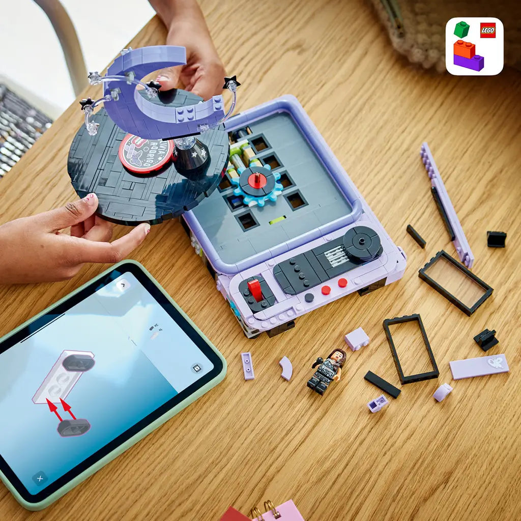 LEGO Olivia Rodrigo Concert Moon in lavender, black and gray bricks is being assembled on a wood table with loose pieces, singer minifigure and digital instructions.