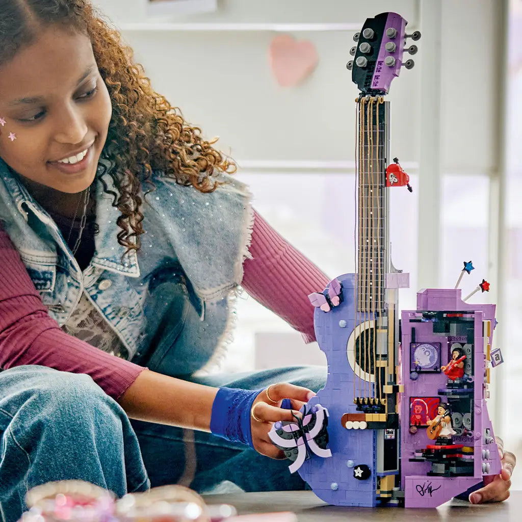LEGO Olivia Rodrigo Dual Guitar in lavender and black bricks opens to reveal a detailed interior as a young builder handles the butterfly feature in a bright room.