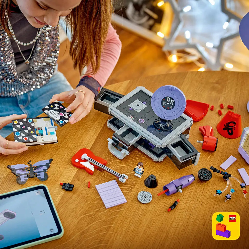 LEGO Olivia Rodrigo Secret Storage in black, gray, lavender and red bricks is spread across a wood table as a builder assembles the music case with digital instructions.