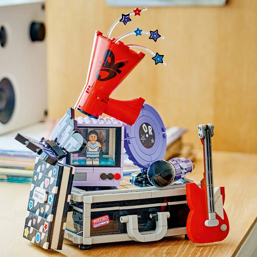 LEGO Olivia Rodrigo Secret Storage in black, gray, lavender and red bricks sits on a wood surface with a red guitar, lavender record, microphone and star-topped megaphone.