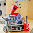 LEGO Olivia Rodrigo Secret Storage in black, gray, lavender and red bricks sits on a wood surface with a red guitar, lavender record, microphone and star-topped megaphone.