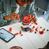 LEGO Ferrari Charles Leclerc helmet building set features red, white and black plastic brick components forming a Formula 1 racing helmet, with a builder assembling panels beside digital instructions on a tabletop.