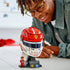 LEGO Ferrari Charles Leclerc helmet display features red, white and black glossy plastic brick construction shaped as a Formula 1 racing helmet on a stand, with a builder admiring the completed collectible model.