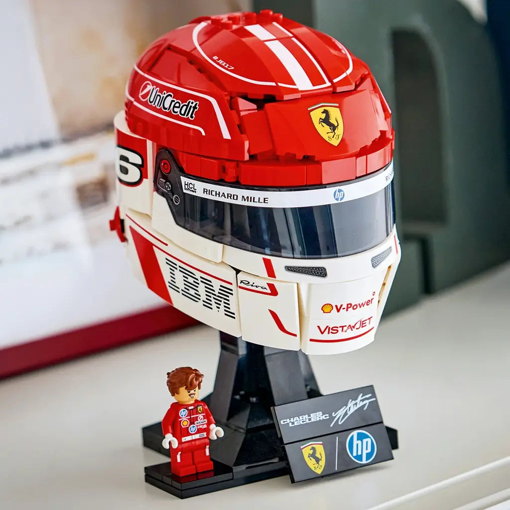 LEGO Ferrari Charles Leclerc helmet collectible features red, white and black glossy plastic brick construction shaped as a Formula 1 racing helmet on a display stand, showcased on a shelf beside the included minifigure.