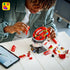 LEGO Ferrari Charles Leclerc helmet model features red, white and black glossy plastic brick construction shaped as a Formula 1 racing helmet on a display stand, shown during assembly with digital instructions and parts on a table.