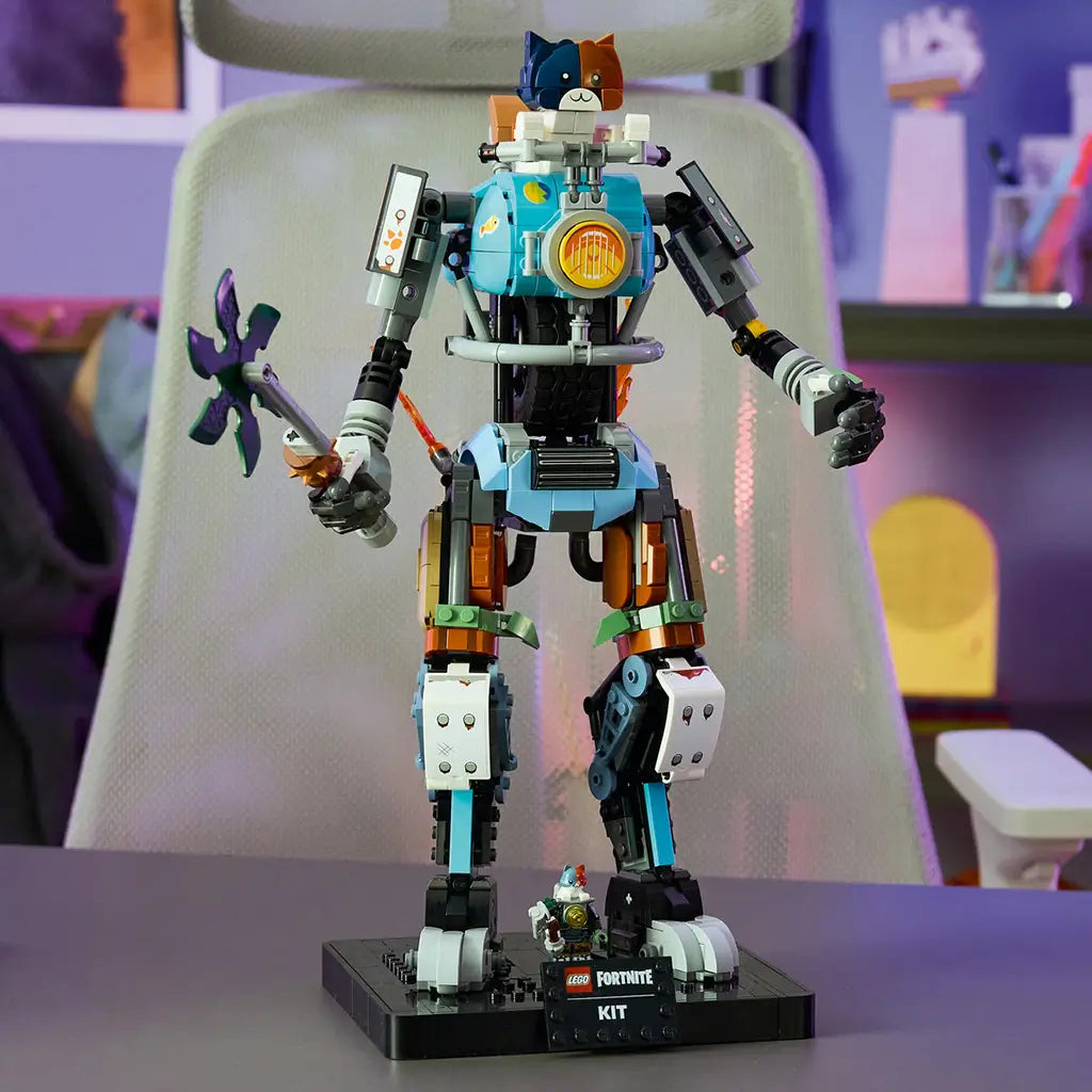 LEGO Fortnite Kit robot in blue, black, gray and brown plastic bricks stands on a black display base with a green pickaxe and small figure in a colorful gaming room.