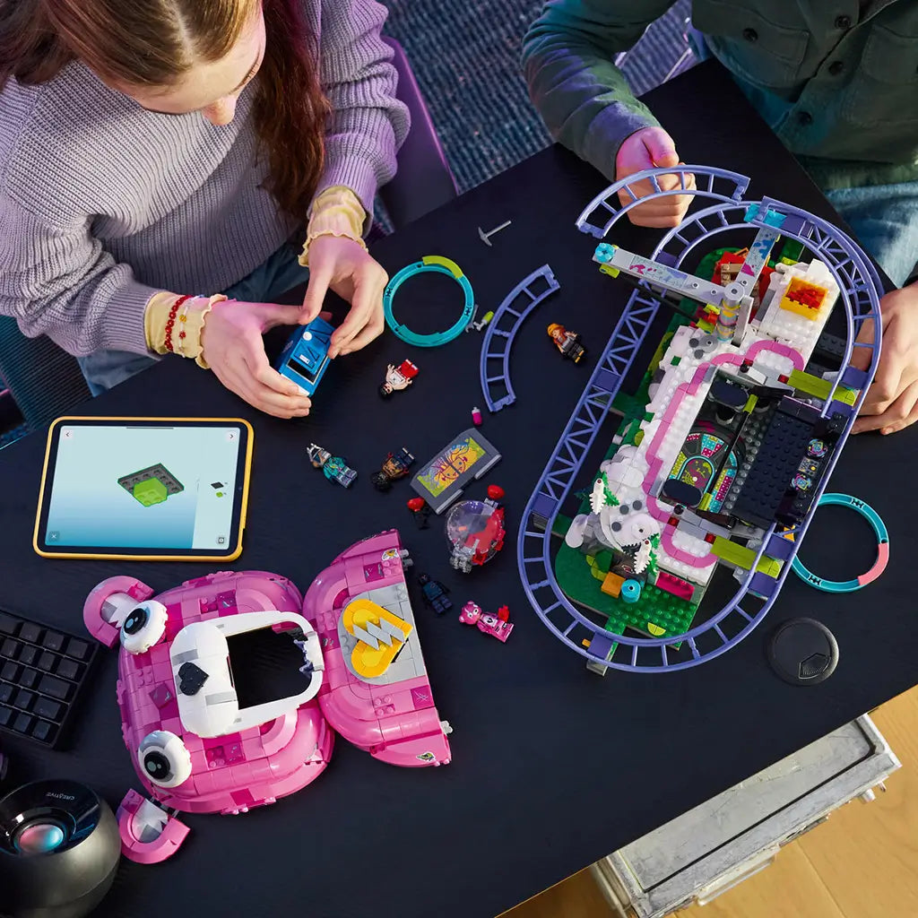 LEGO Fortnite Rave Cave in pink, white and purple plastic bricks is assembled by two builders at a black table, with rail sections, minifigures and digital instructions nearby.
