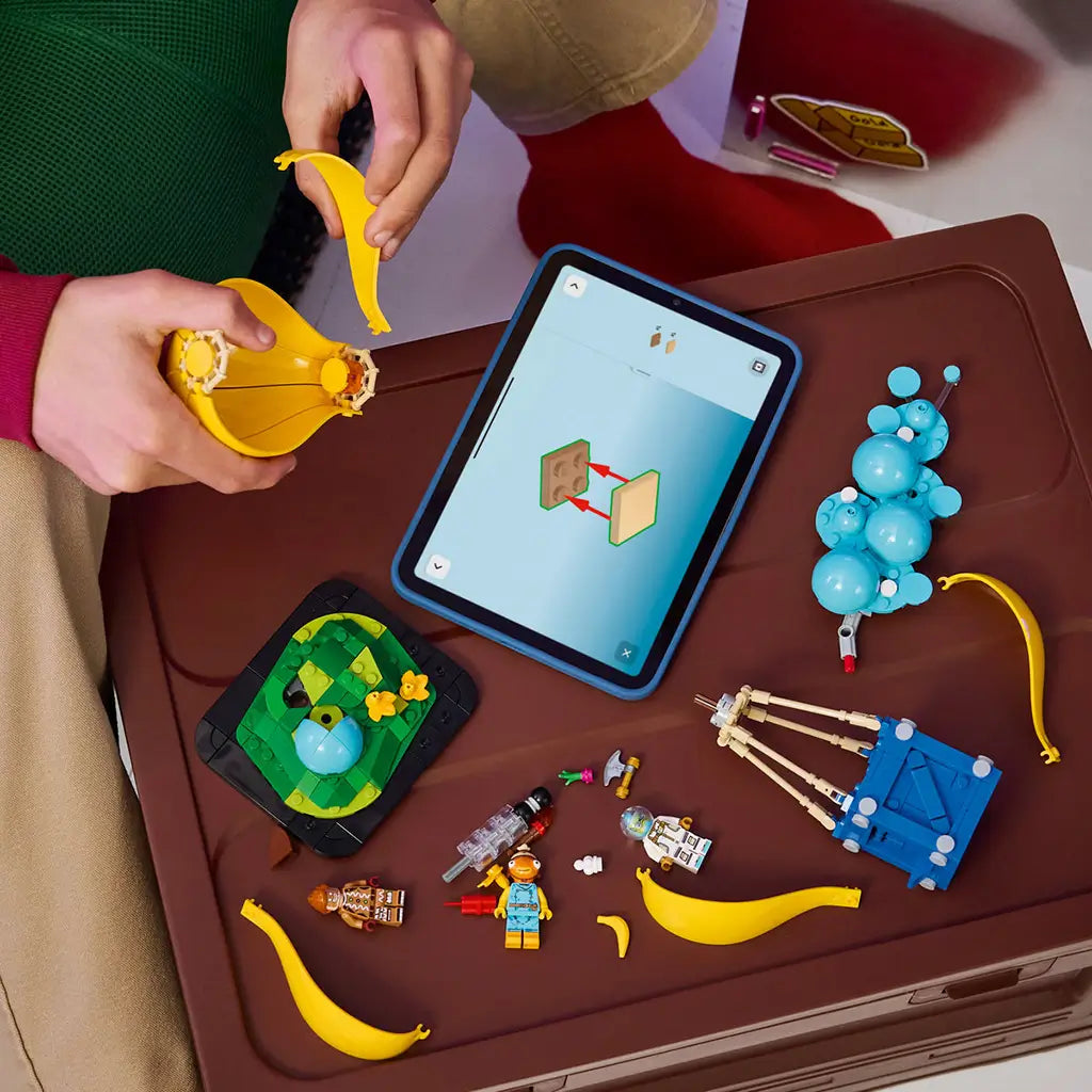 LEGO Fortnite Supply Drop set in yellow, blue and turquoise plastic bricks is assembled beside digital instructions, with balloon panels, figures, accessories and terrain pieces.
