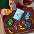 LEGO Fortnite Supply Drop set in yellow, blue and turquoise plastic bricks is assembled beside digital instructions, with balloon panels, figures, accessories and terrain pieces.