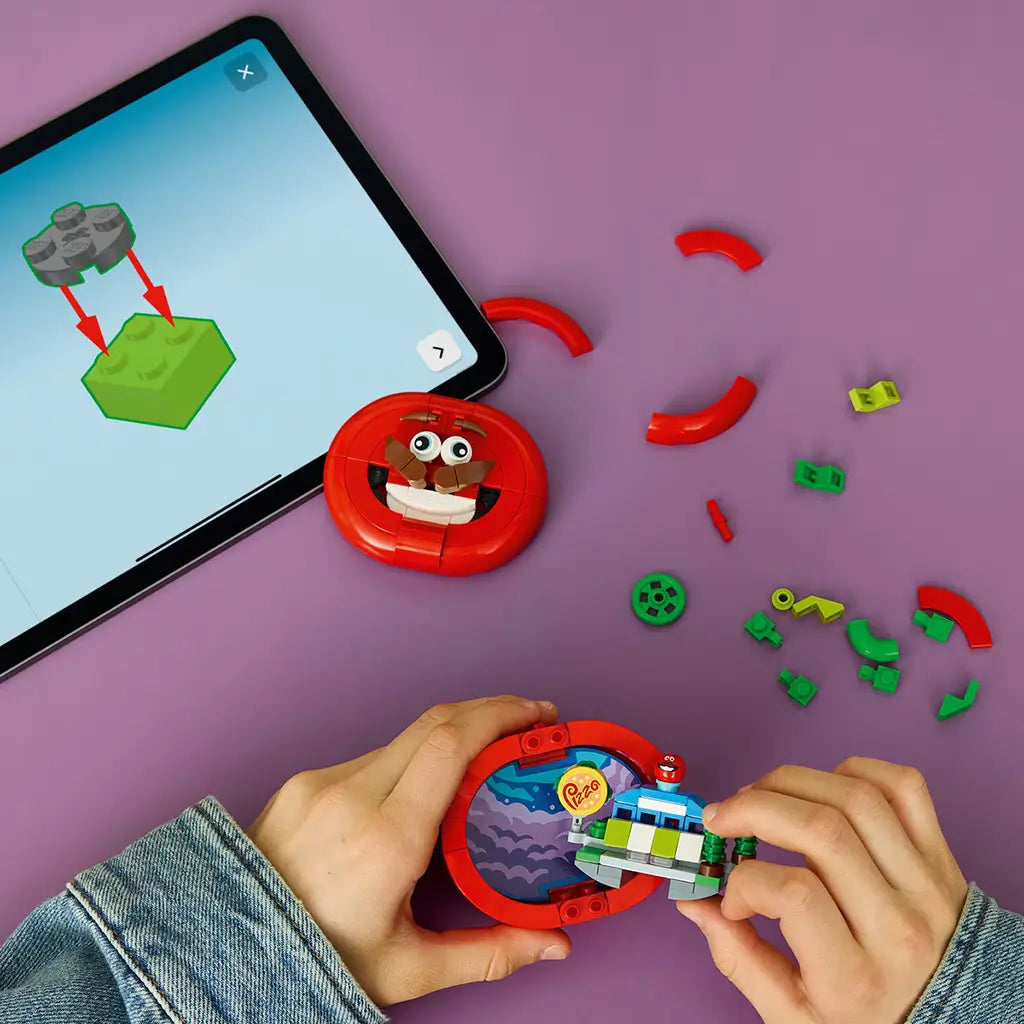 LEGO Fortnite Tomatohead set in red, green and brown plastic bricks is assembled beside digital instructions, with the tomato shell opened to reveal a colorful interior scene.