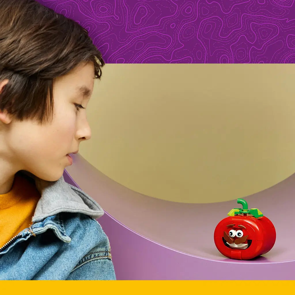 LEGO Fortnite Tomatohead set in red, green and brown plastic bricks sits on a curved purple shelf as a child looks toward the smiling tomato display in a colorful room.