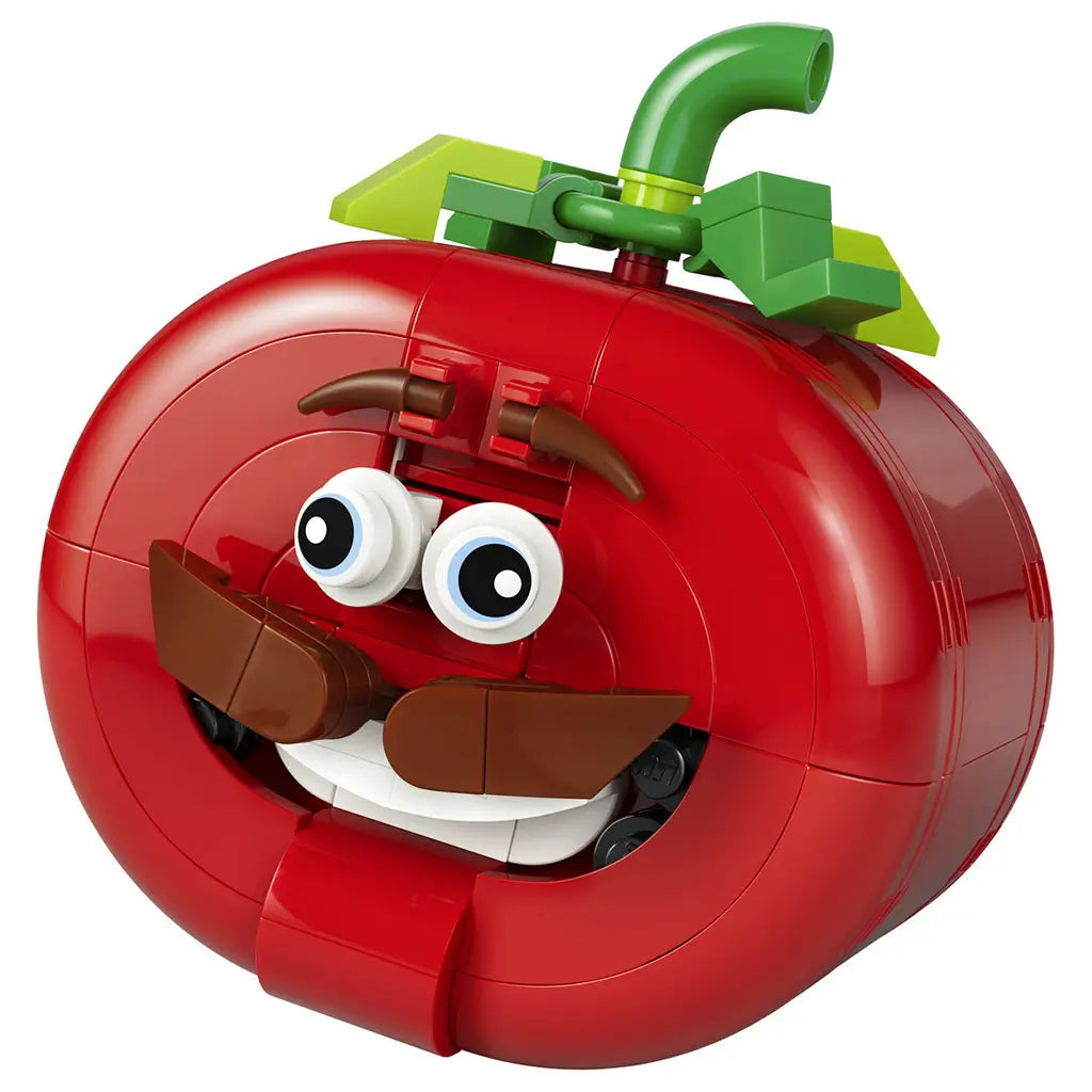 LEGO Fortnite Tomatohead set in red, green and brown plastic bricks, shaped as a smiling tomato head with wide eyes, mustache, white teeth and leafy stem on white.